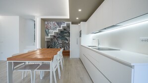 A modern kitchen with white cabinetry, a wooden dining table, and a staircase leading to another level.