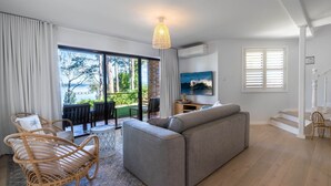 A modern living room with a grey sofa, wicker chairs, a TV, and a view of the outdoors. - Waterfront Getaway, Kayaks included in stay - Kid Friendly (Sanctuary Point)