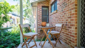 A small patio with two wooden chairs and a table, a potted plant, and a brick wall.