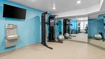 Uma academia moderna com equipamentos de ginástica, um bebedouro e um espelho grande refletindo o ambiente.