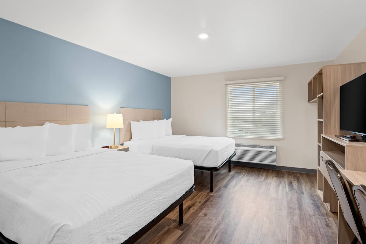 Habitación de hotel con dos camas, televisión, escritorio y ventana con persianas.