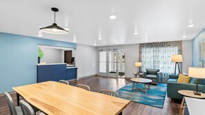 Una habitación de hotel moderna con una mesa de comedor de madera, un sofá, una pequeña mesa de centro y una lámpara.