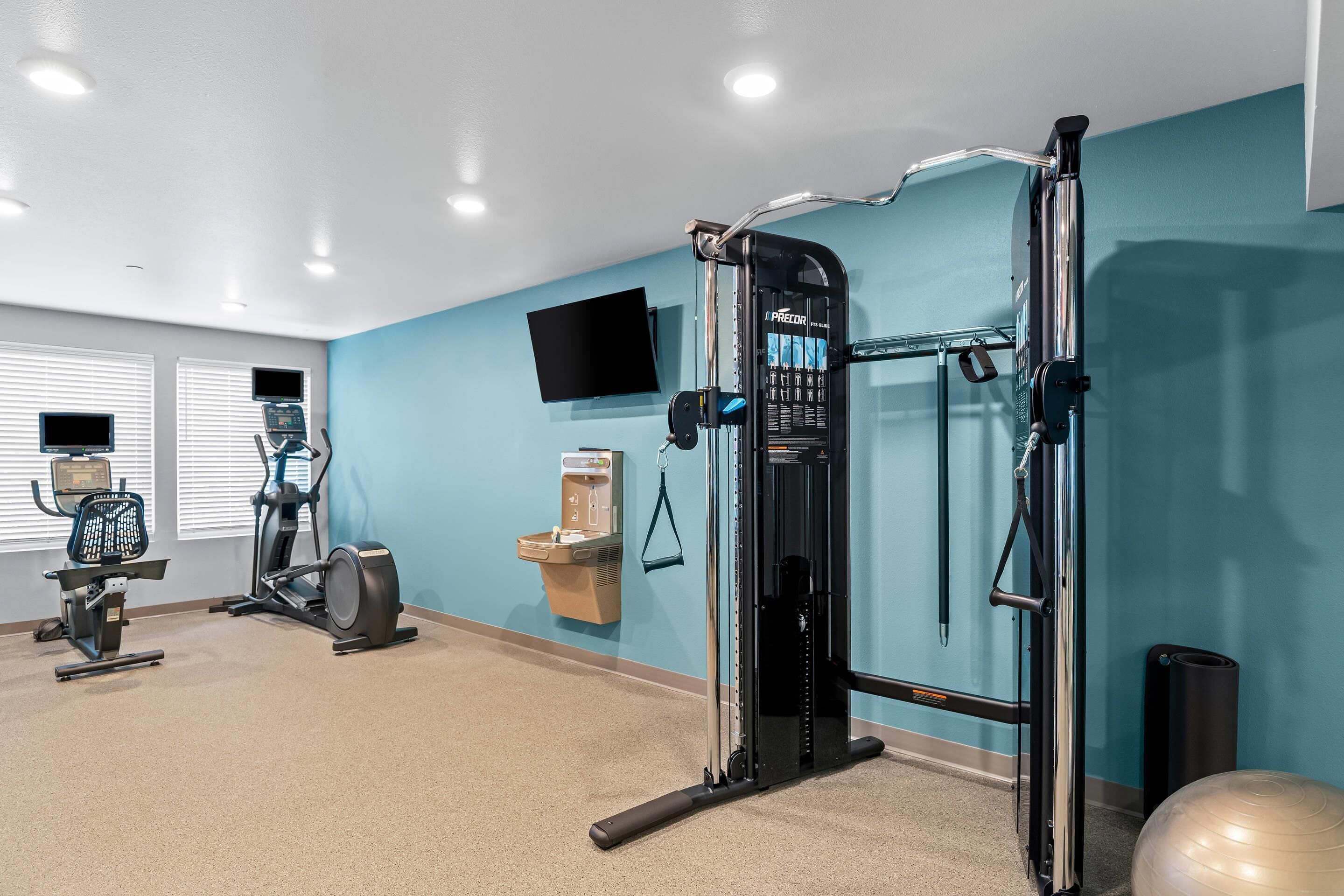 A gym with exercise equipment, a TV, and a water dispenser.