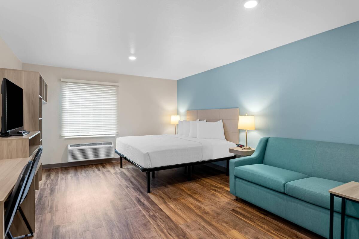 Una habitación de hotel con cama, escritorio, televisor, sofá y dos lámparas de noche.