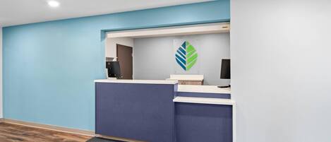 A reception area with a blue and white color scheme, a reception desk, a logo on the wall, and a carpeted floor.