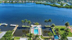 An aerial view of a waterfront property with a central swimming pool, docked boats, and lush greenery. - Palm Bay Club Private Balcony Beach Side  (Sarasota)