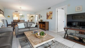 A living room with a sofa, coffee table, TV stand, and a dining area with chairs and a table. - Palm Bay Club Private Balcony Beach Side  (Sarasota)