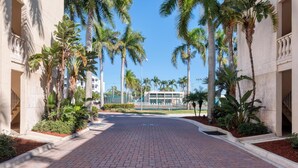 A paved walkway flanked by palm trees and a building with a modern design. - Palm Bay Club Private Balcony Beach Side  (Sarasota)