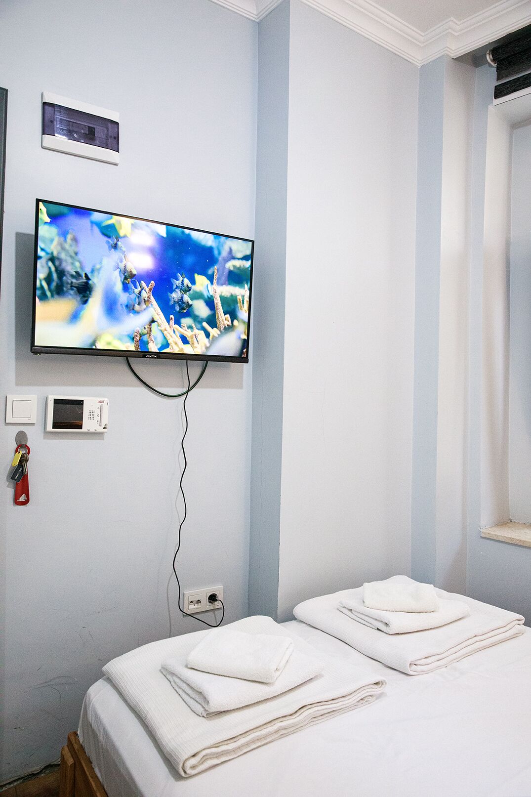 A hotel room with a television mounted on the wall, a bed with white linens, and a window with curtains.