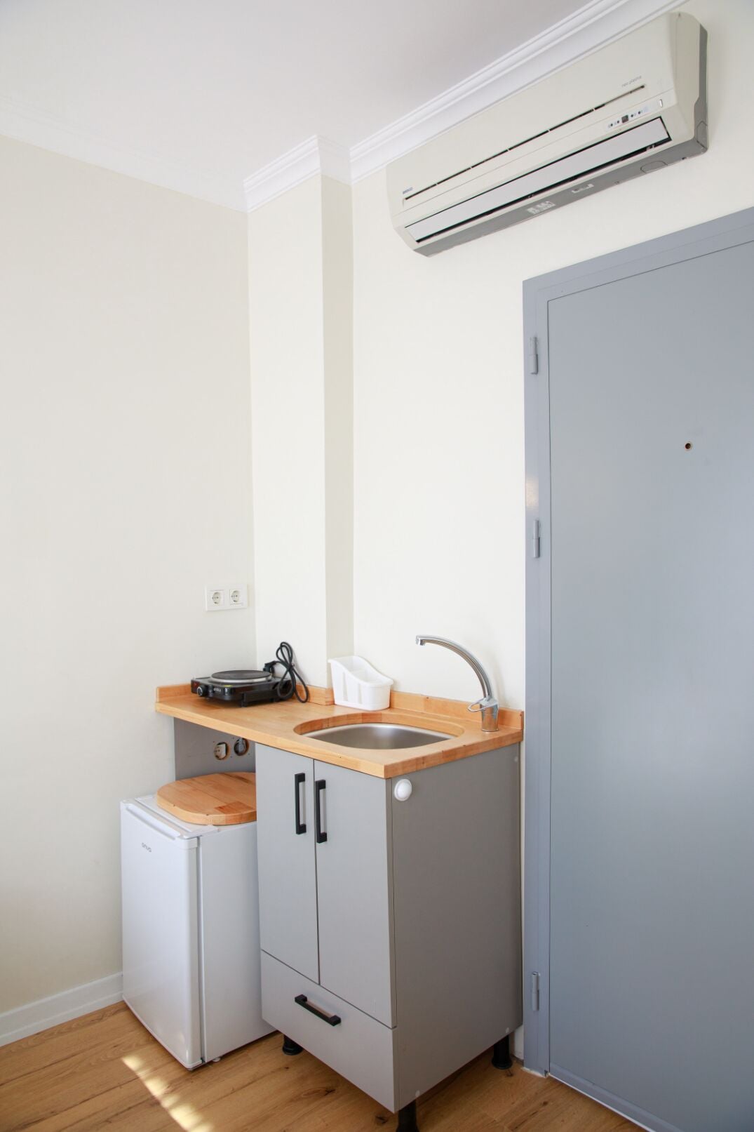 Una cocina compacta con un lavamanos, un refrigerador pequeño y un aire acondicionado instalado en la pared.