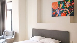 A modern hotel room with a large bed, a gray headboard, and a colorful abstract painting on the wall.