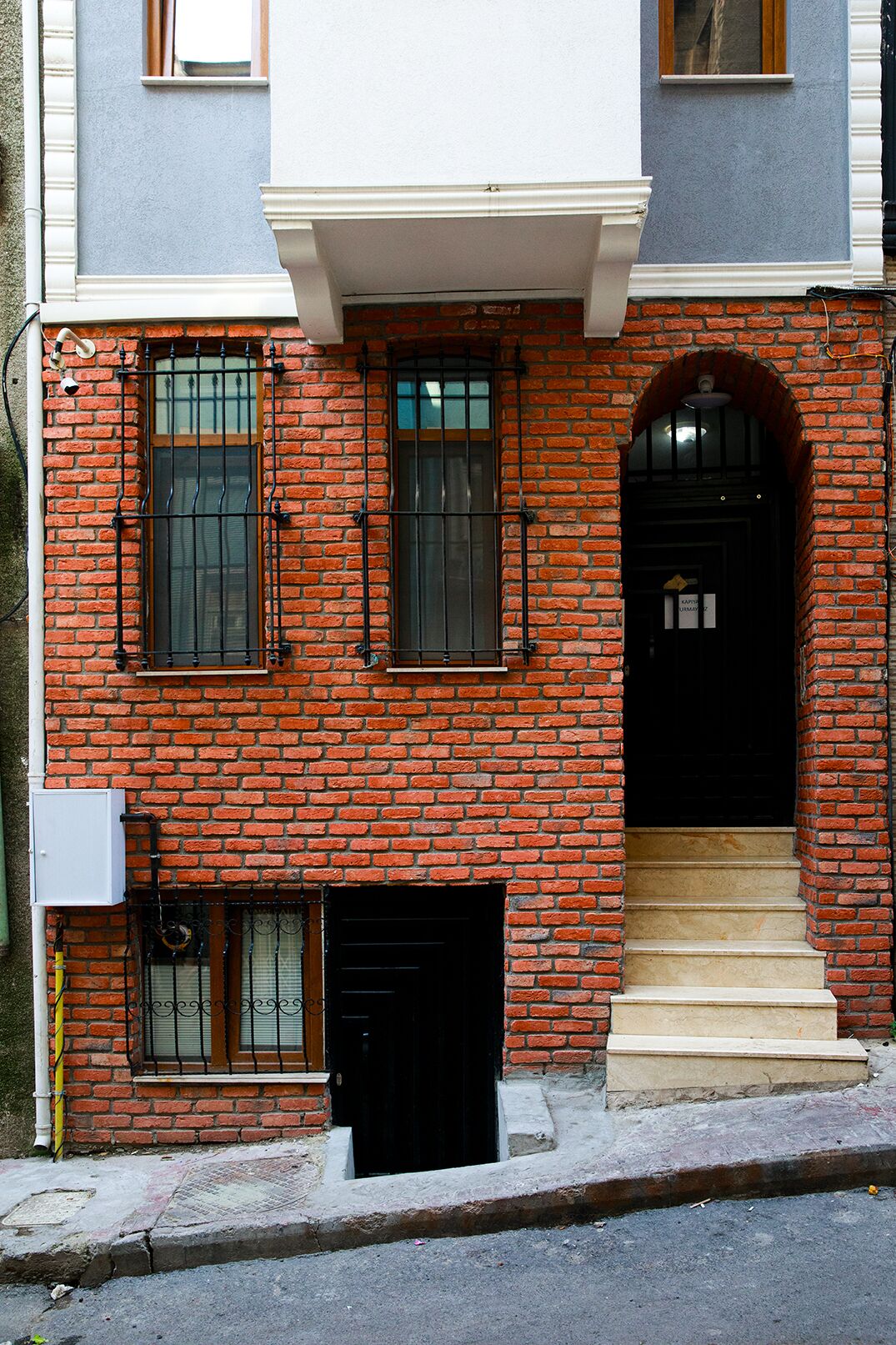 A two-story brick building with a black front door and a small set of beige steps leading to the entrance.
