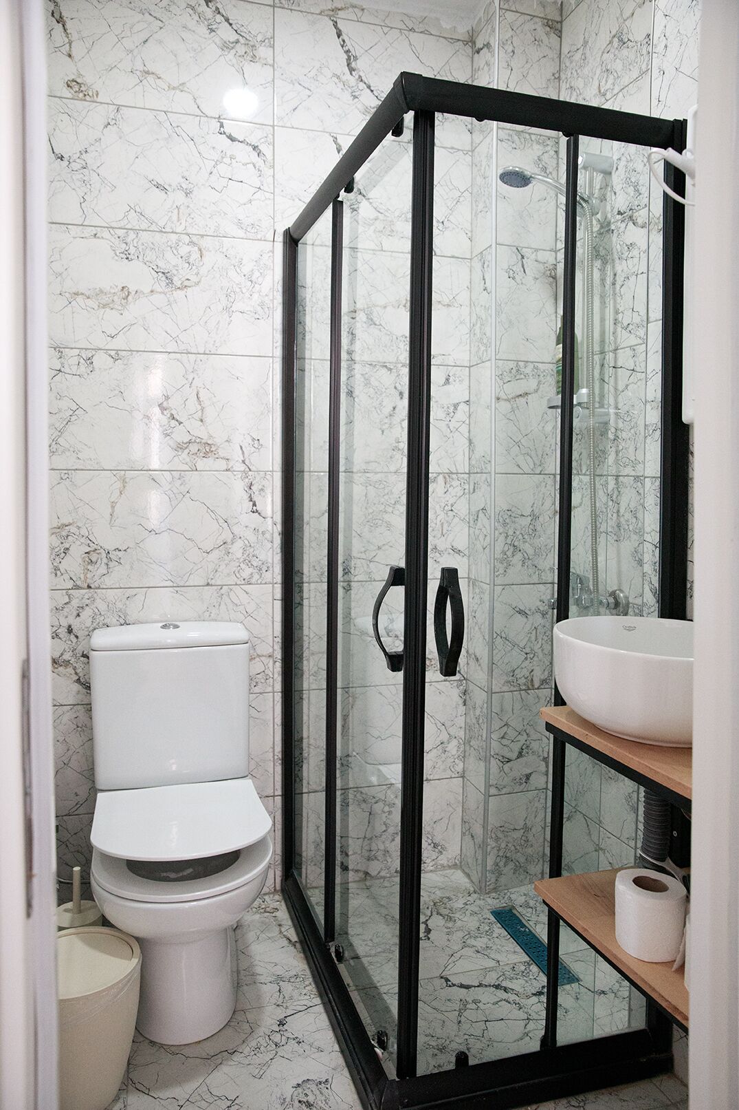 A bathroom with a glass-enclosed shower, a toilet, and a sink with a marble backsplash.