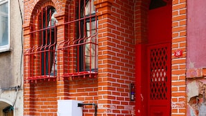 A red brick building with a white door, a red mailbox, and a number '26' sign.