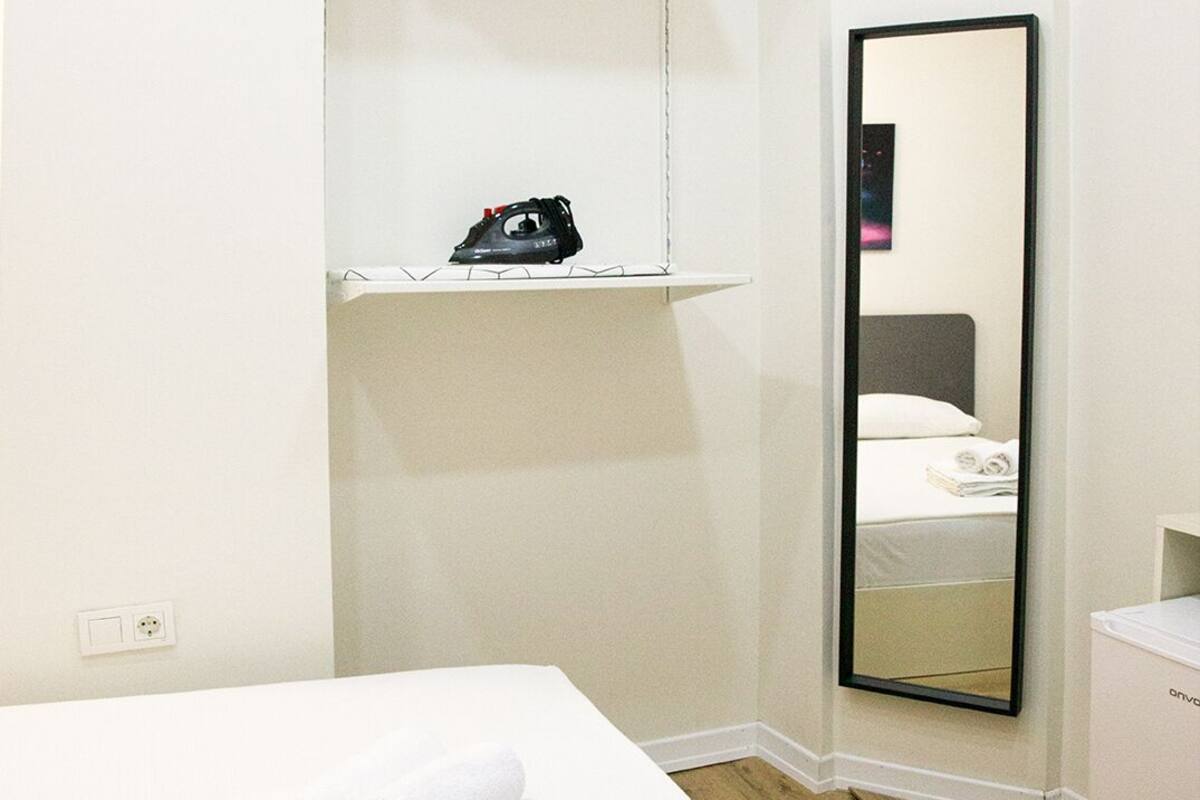 A hotel room with a bed, a mirror, a shelf with a shoe, and a small white cabinet.