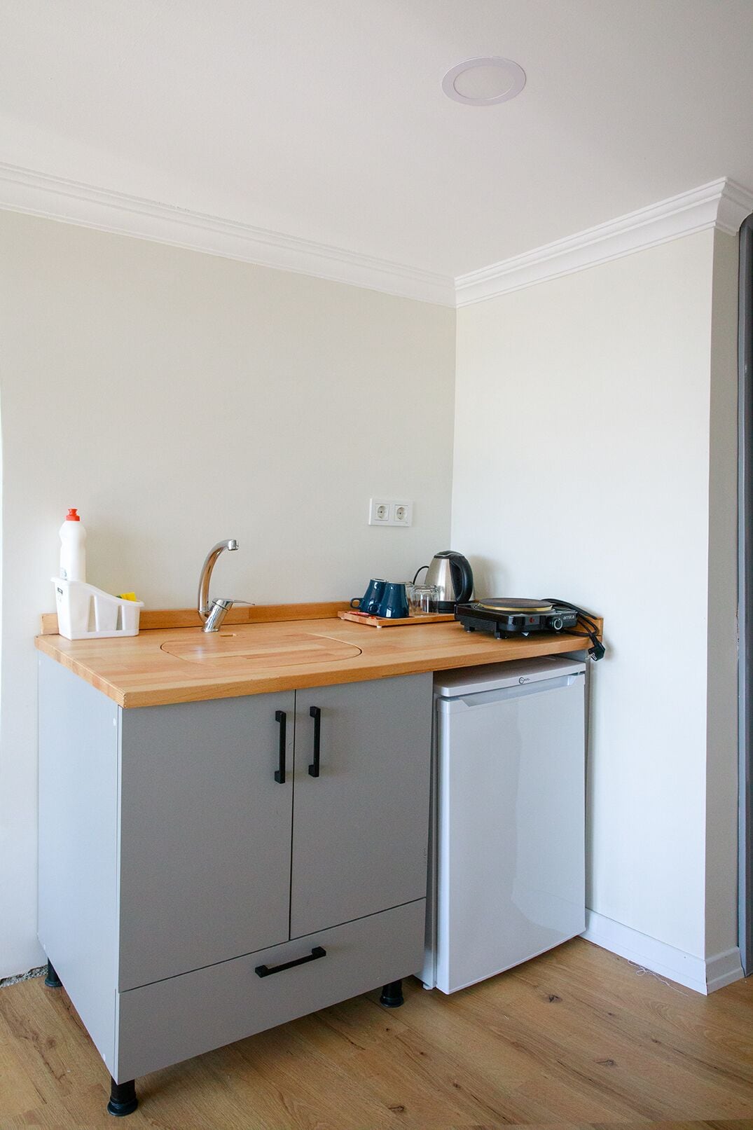 Una cocina compacta con encimera de madera, un lavamanos, un hervidor y un lavavajillas pequeño.