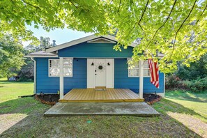 Uma casa pequena azul com porta branca, varanda de madeira e uma bandeira americana.
