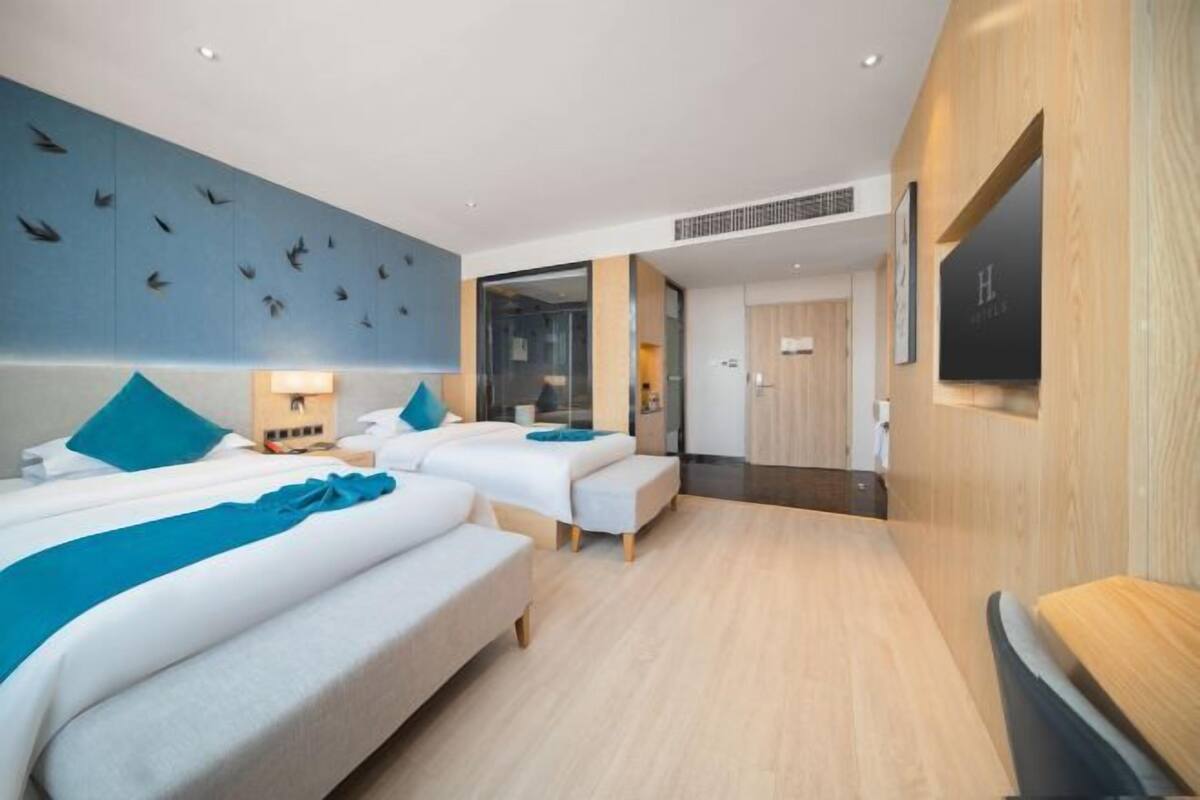 A hotel room with two beds, a large mirror, a wooden floor, and a wall with a bird mural.
