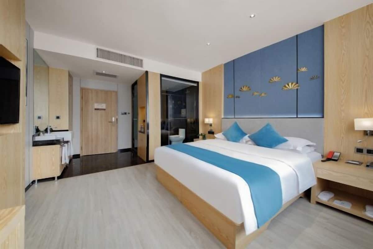 A modern hotel room with a large bed, a wooden wardrobe, a flat-screen TV, and a bathroom visible through an open door.