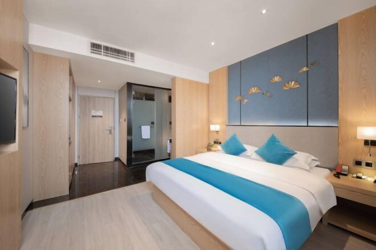 A modern hotel room with a large bed, a flat-screen TV, a wooden wardrobe, and a wall-mounted artwork.