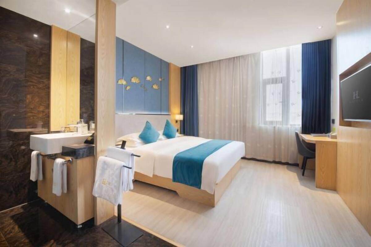 A hotel room with a bed, a desk, a TV, a bathroom with a sink, and a mirror.
