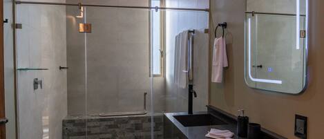 A modern bathroom with a glass-enclosed shower, a vanity with a sink, and a mirror.
