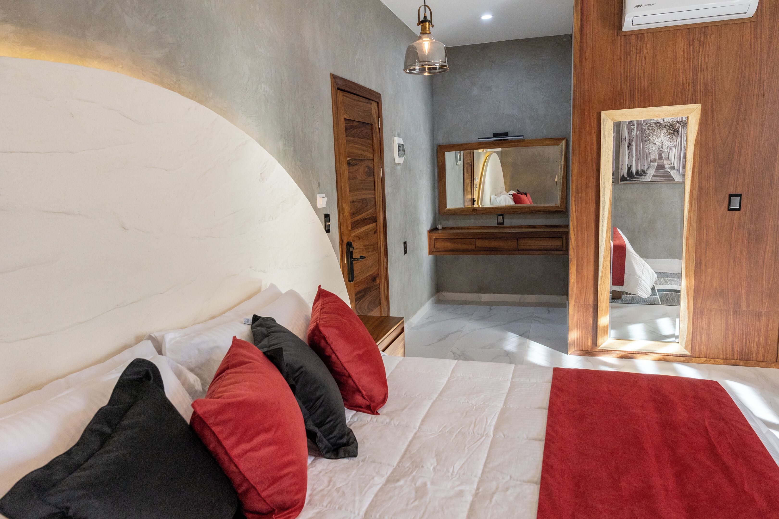 Un dormitorio con una cama grande, una puerta de madera, un espejo y vista a un pasillo.