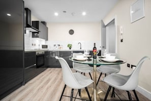 A modern kitchen with a glass dining table, white chairs, and a wine bottle. - Two Bed Apartment - Smart TV - WIFI - Jewellery Quarter (Birmingham)