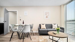 Un salon moderne avec un canapé gris, une table basse ronde et un coin repas comprenant une table et des chaises en verre.