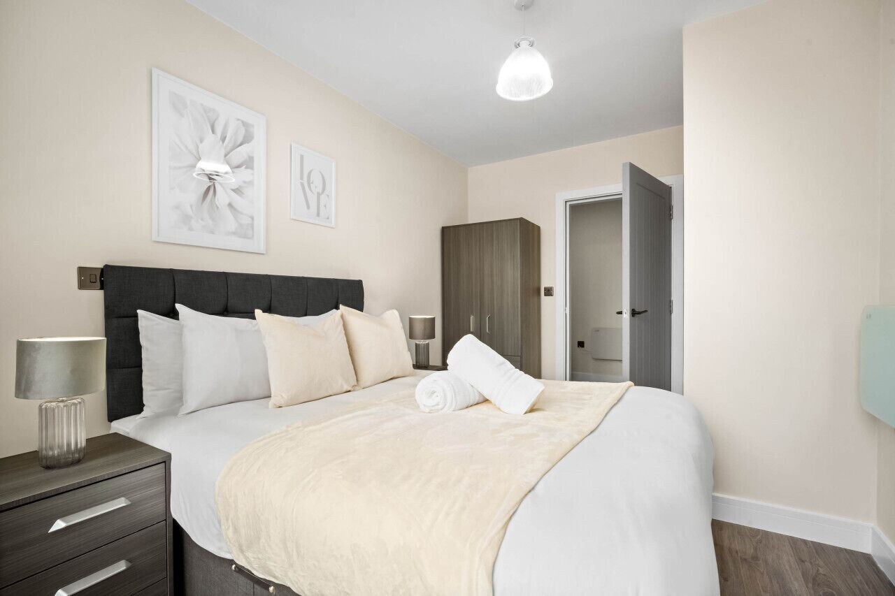 A neatly arranged bedroom with a large bed, a bedside table with a lamp, and a wardrobe.