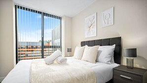 Habitación de hotel con una cama grande, una mesita de noche, una lámpara y dos cuadros en la pared.