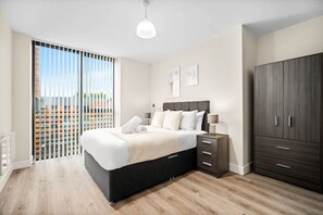 A modern bedroom with a large bed, a wardrobe, a bedside table, and a view through a sliding door.