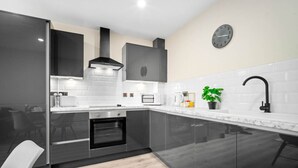Una cocina moderna con armarios oscuros, una encimera blanca, un extractor de aire negro, un reloj en la pared y una planta en maceta.