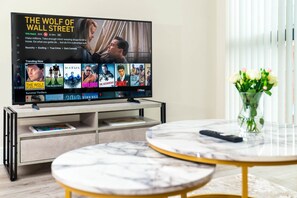 Ein modernes Wohnzimmer mit einem Flachbildfernseher, der einen Film zeigt, einem Couchtisch und einer Vase mit Blumen.