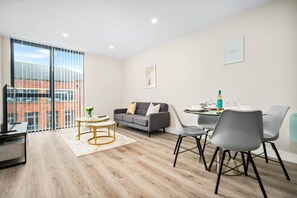 A modern living room with a sofa, a coffee table, and a dining area with chairs and a table. - Stylish 2 Bed Apartment - Smart TV - WIFI -  Jewellery Quarter (Birmingham)