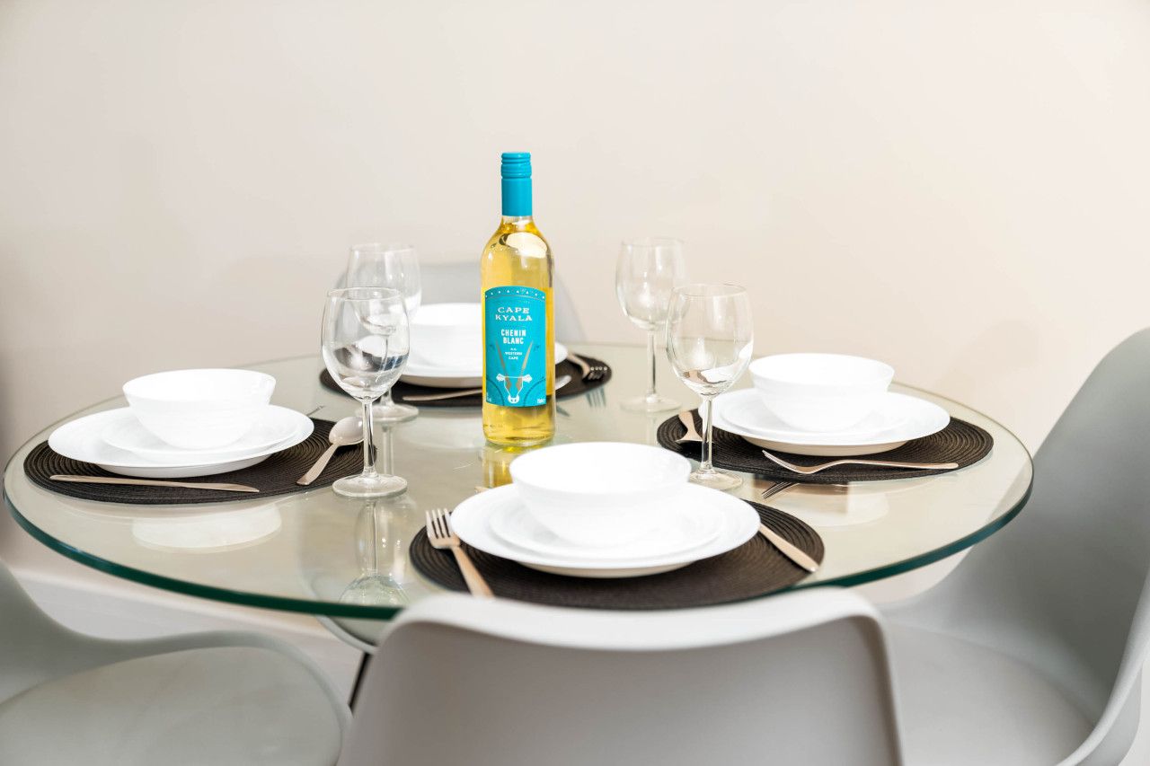A dining table set with white plates, cutlery, and a bottle of wine.