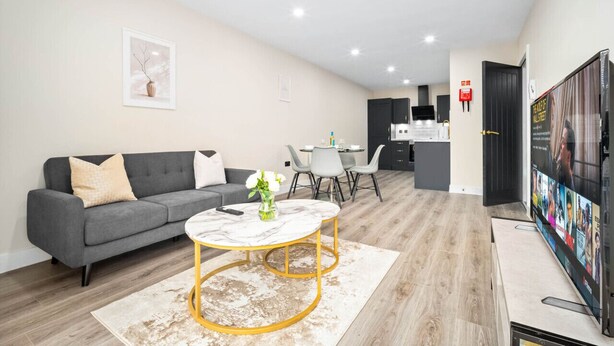 A modern living room with a grey sofa, a marble coffee table, and a dining area with a small table and chairs.
