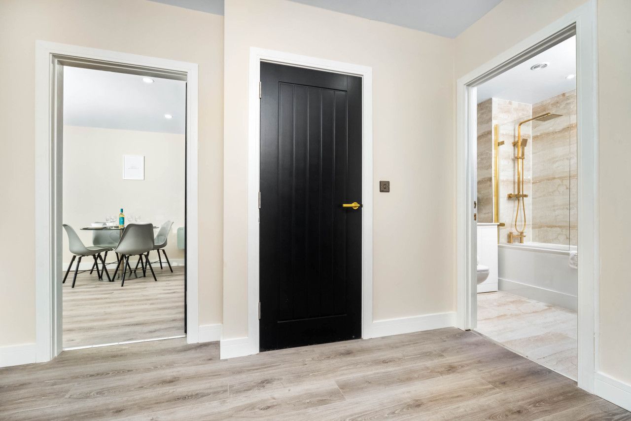 A hallway with a black door, a dining area with a table and chairs, and a bathroom with a shower and bathtub.