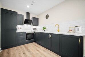 Une cuisine moderne avec des meubles de couleur sombre, des plans de travail blancs et un plancher en bois.