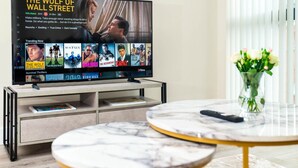 A modern living room with a flat-screen TV displaying a movie, a coffee table, and a vase with flowers.