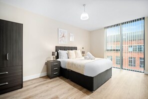 A bedroom with a bed, bedside tables, a wardrobe, and a large window with a view of buildings. - Stylish 2 Bed Apartment - Smart TV - WIFI -  Jewellery Quarter (Birmingham)