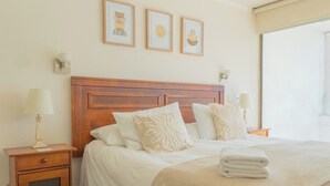 A hotel room with a wooden headboard, two bedside lamps, a nightstand, a bed with white bedding and decorative pillows, and three framed artworks on the wall. - Charming 2-bedroom apartment with AC, WiFi in Parque Arauco (Vitacura)