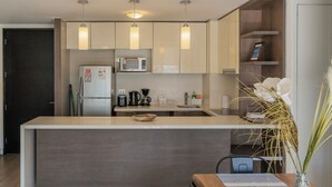 A modern kitchen with a central island, built-in microwave, and pendant lighting. - Charming 2-bedroom apartment with AC, WiFi in Parque Arauco (Vitacura)