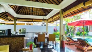 A covered outdoor area with a dining table, chairs, a bar area, and a poolside lounge with umbrellas. - Imani Villas Bali (Bali)