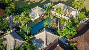 An aerial view of a resort with a swimming pool surrounded by palm trees and bungalow-style buildings. - Imani Villas Bali (Bali)