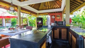 An outdoor kitchen area with a dining table set for two, a built-in microwave, and a sink. - Imani Villas Bali (Bali)