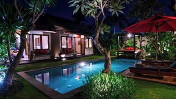 A poolside area with a lounge chair, a red umbrella, and a building with glass doors.