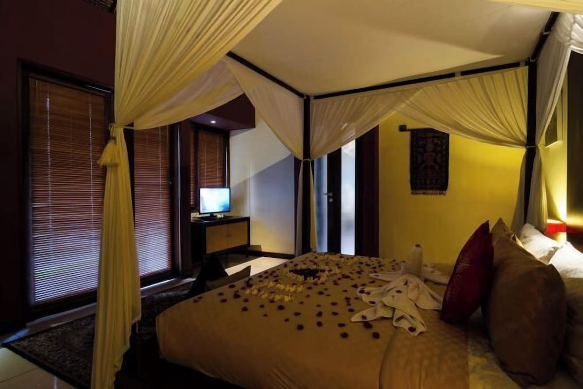 A hotel room with a bed, curtains, a desk, and a television.