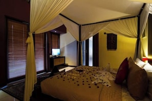 A hotel room with a bed, curtains, a desk, and a television. - Imani Villas Bali (Bali)