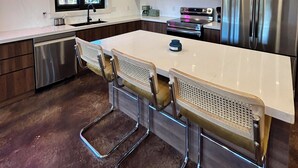 Una cocina moderna con una isla grande, electrodomésticos de acero inoxidable e iluminación colgante.